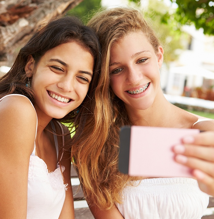 Two teen girls smiling one has traditional braces
