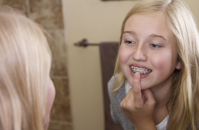 Young girl with pediatric orthodontics pointing to her smile