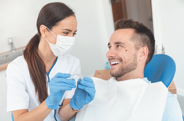 Man smiling at dentist holding a clear aligner