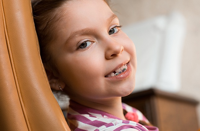 Young girl receiving pediatric orthodontic treatment smiling in orthodontic chair