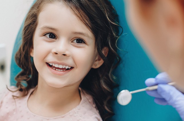 Young girl in orthodontic chair smiling at orthodontist during pediatric orthodontic treatment