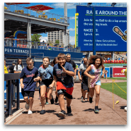 Large group of kids running around baseball field