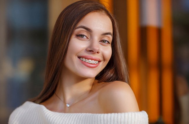 Young woman in cream sweater smiling with braces