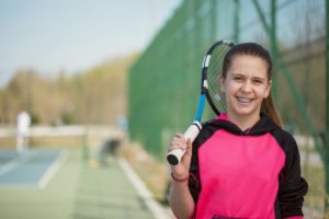 Girl with tennis racket smiles after playing sports with braces