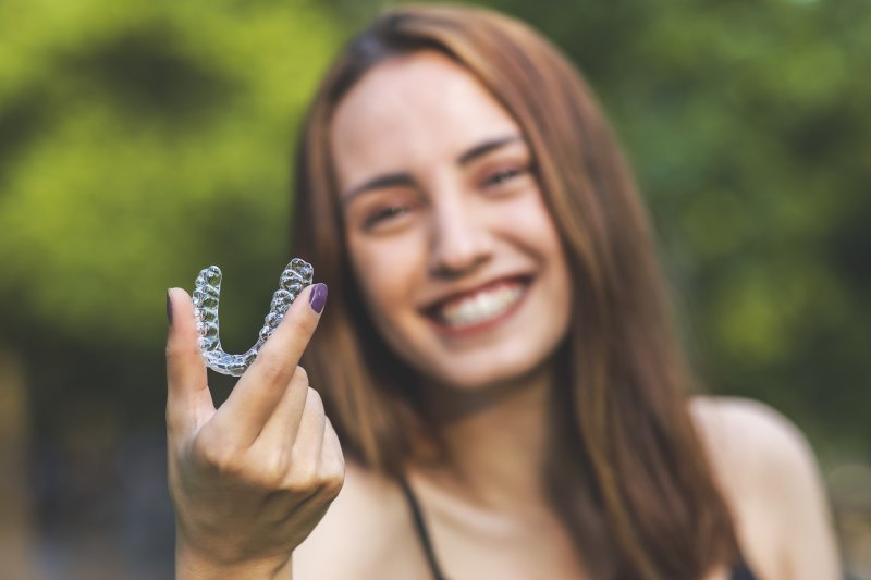 Woman smiling while holding up Invisalign aligner