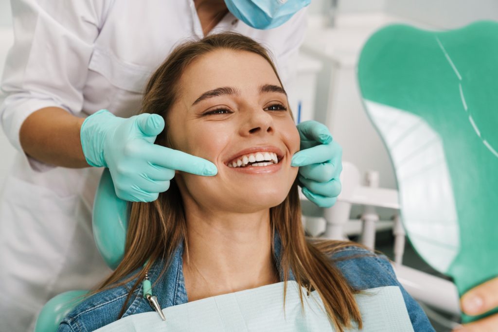 Woman smiling in orthodontist's mirror after braces removal