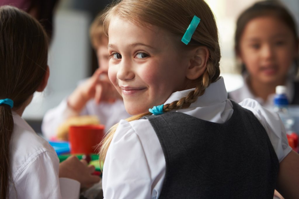 Closeup of young girl smiling while eating lunch in cafeteria