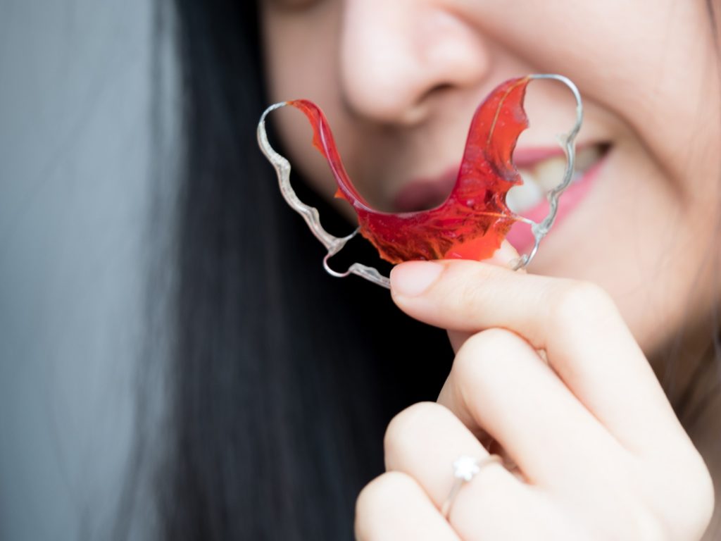 Woman smiling while holding up red retainer